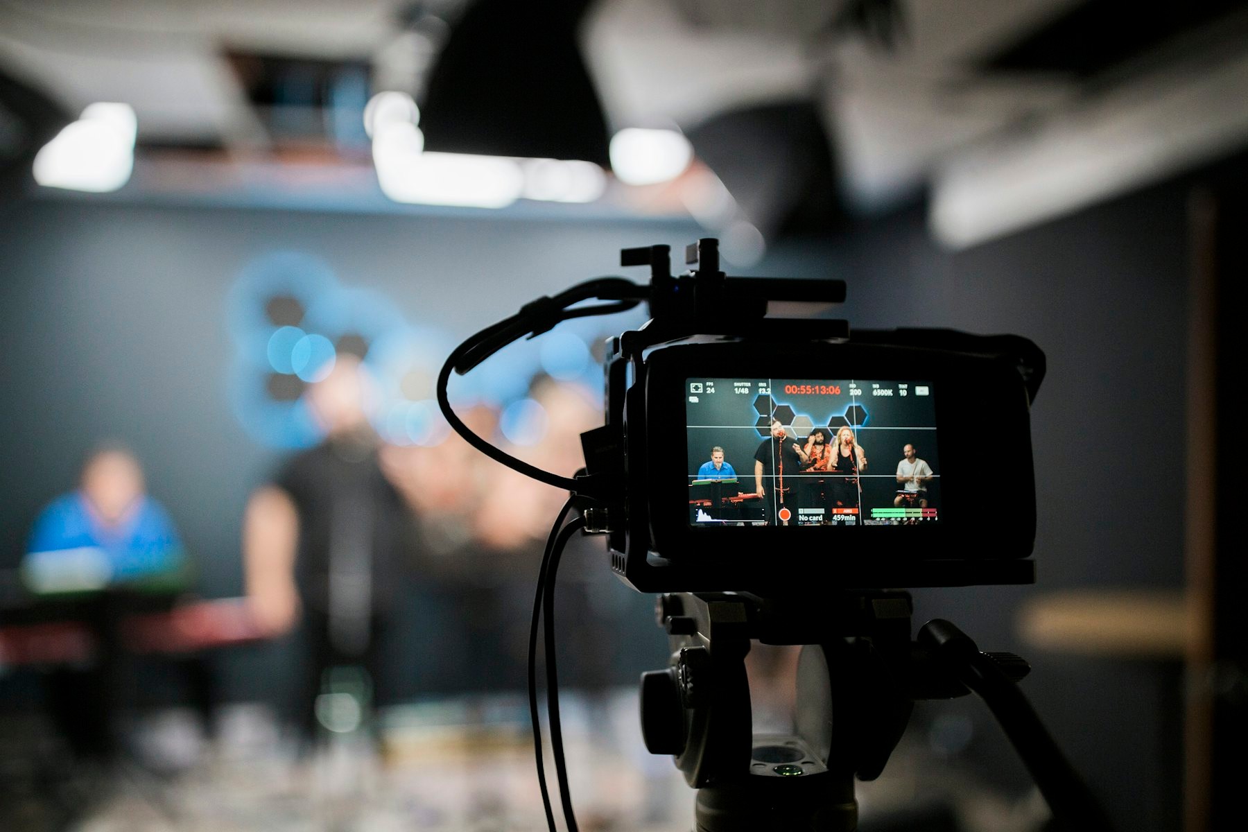 A professional video camera recording a group performing in a studio.