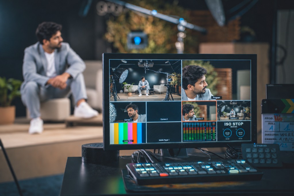 A control-desk monitor showing four camera feeds, with the studio set behind it.