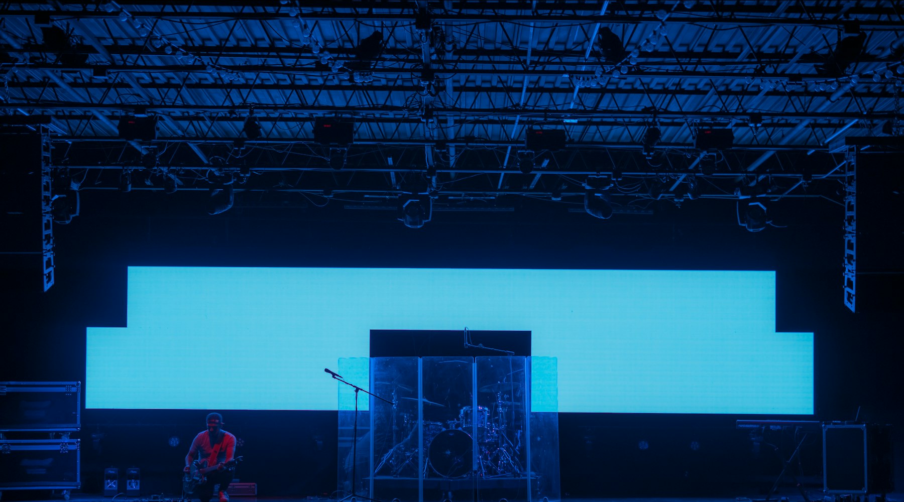A large illuminated screen wall on a stage, beneath a lighting truss.