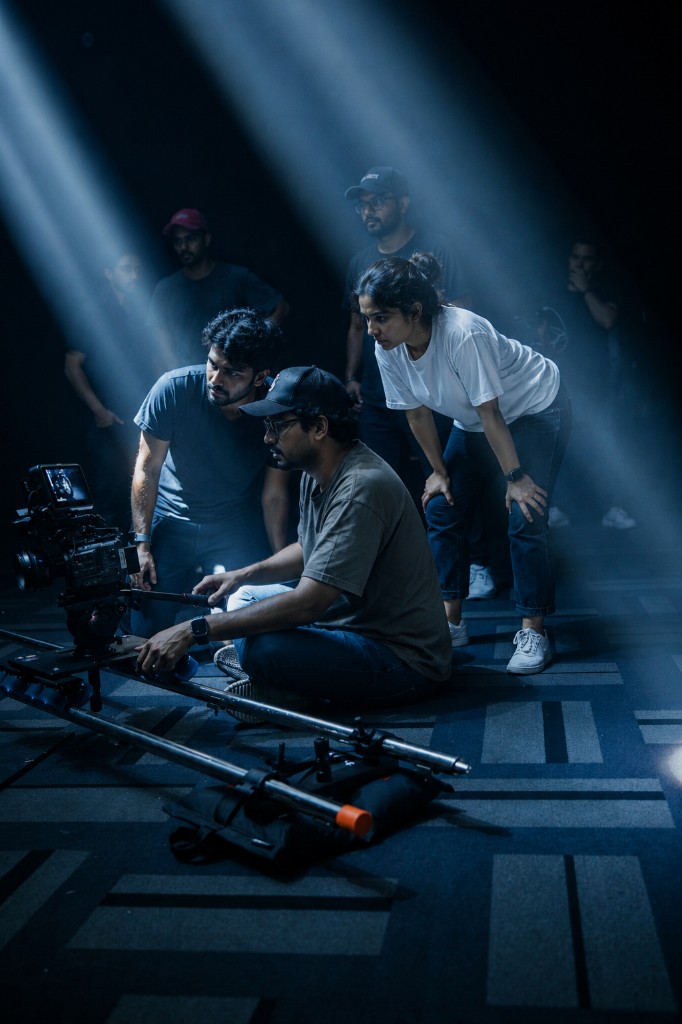 A film crew on a dark stage, gathered around a camera on a floor slider.