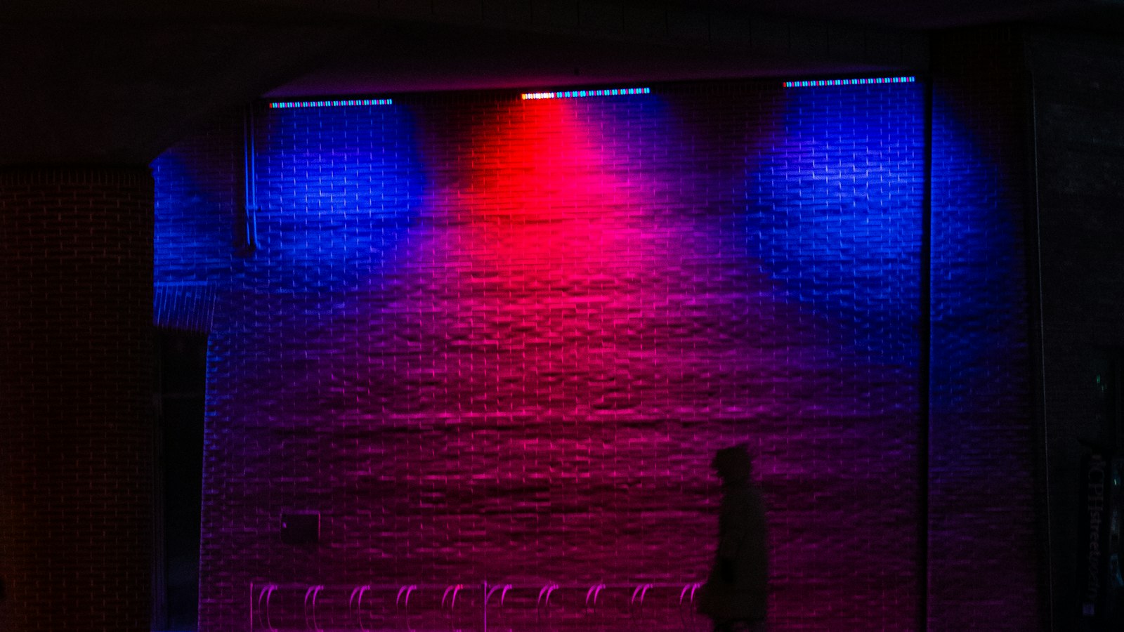 A performer standing in front of a large wall lit in red and blue.